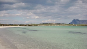 Ein Strand mit klarem türkisblauem Wasser, einem Sandstrand und einem entfernten Berg.
