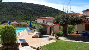 Ein Poolbereich mit Liegestühlen und Sonnenschirmen, umgeben von einer Steinterrasse und einer Rasenfläche.