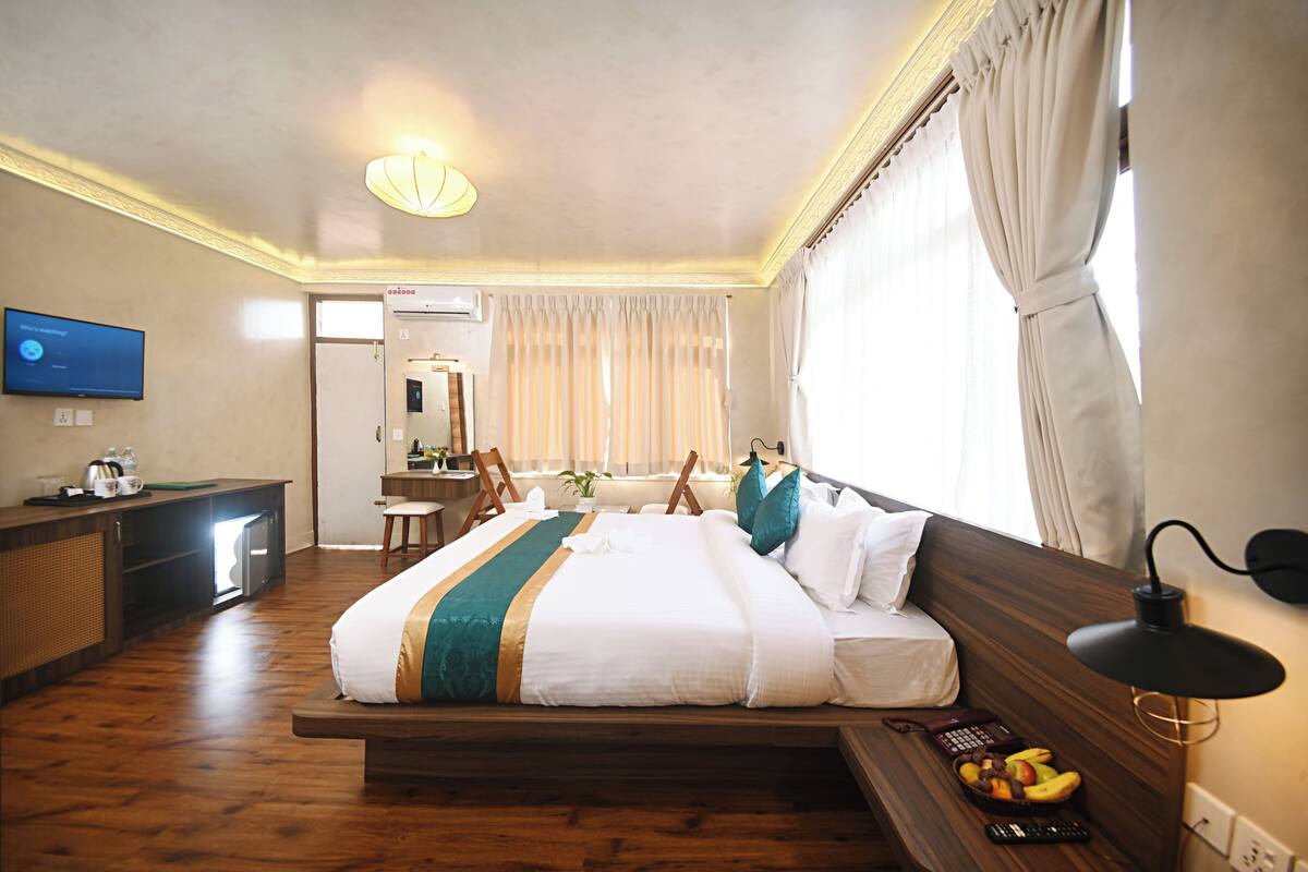 A hotel room with a wooden bed, a desk with a computer, a television, and a fruit basket on the bedside table.