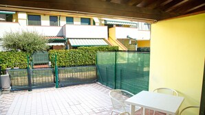 Ein Terrassenbereich mit Fliesenboden, einem weißen Tisch und zwei Korbstühlen.