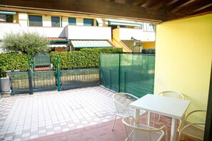 Un'area patio con pavimento piastrellato, un tavolo bianco e due sedie in vimini.