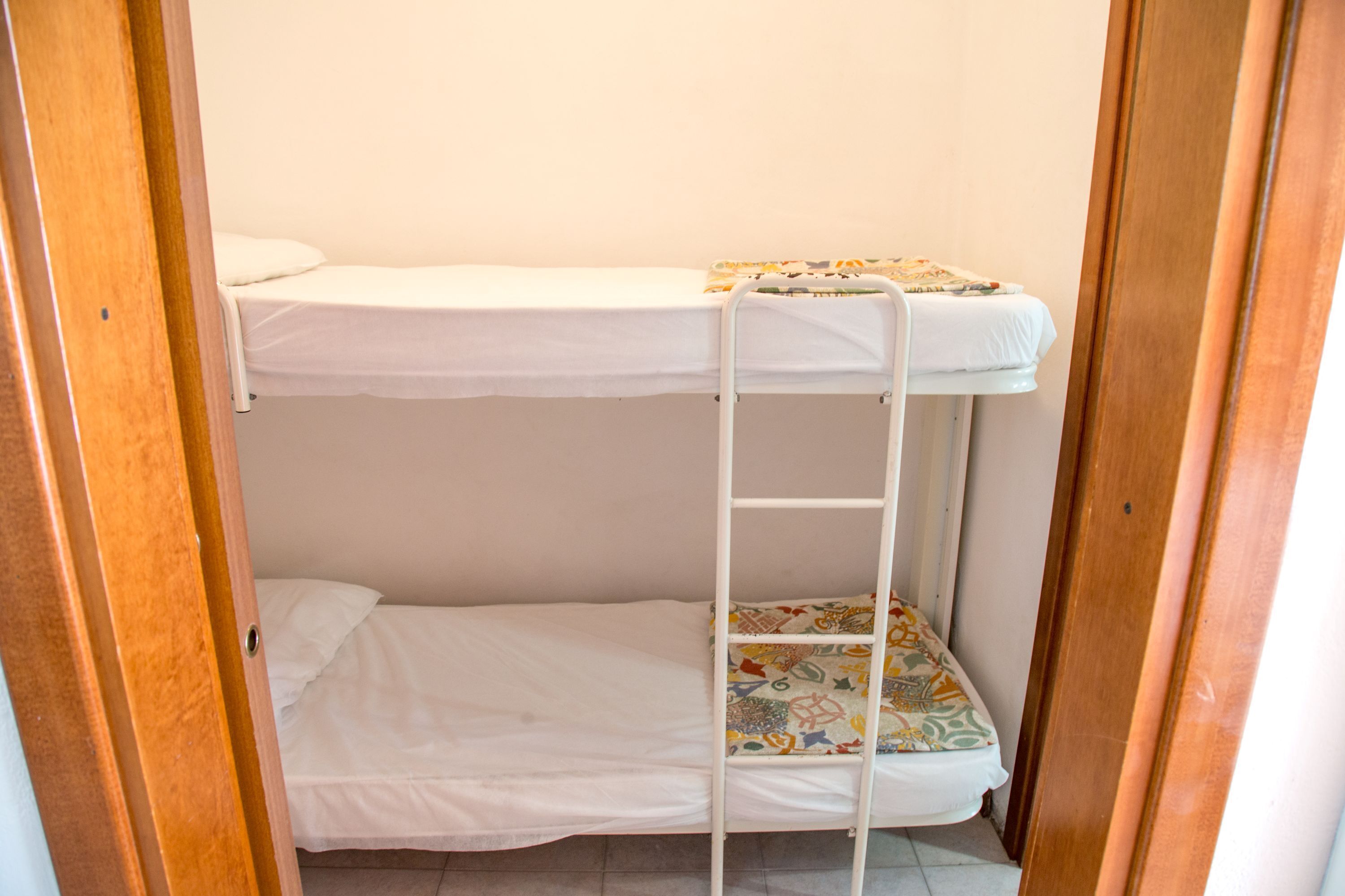 Une chambre avec un lit superposé, une échelle, du linge de lit blanc et un tapis coloré sur le lit du bas.