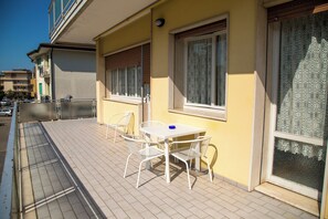 En balkon med et bord og stole, et vindue med rullegardiner og et mønstret gardin.
