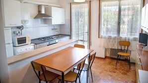 Une cuisine compacte avec une table et des chaises en bois, un four à micro-ondes, une cuisinière et une fenêtre avec des rideaux.