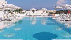 Ein großer Pool mit Liegestühlen und Sonnenschirmen, umgeben von einem weißen Gebäude.
