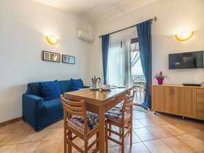 A cozy living room with a wooden dining table, blue sofa, and a TV mounted on the wall.