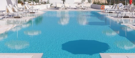 A large swimming pool with lounge chairs and umbrellas, surrounded by a white building.