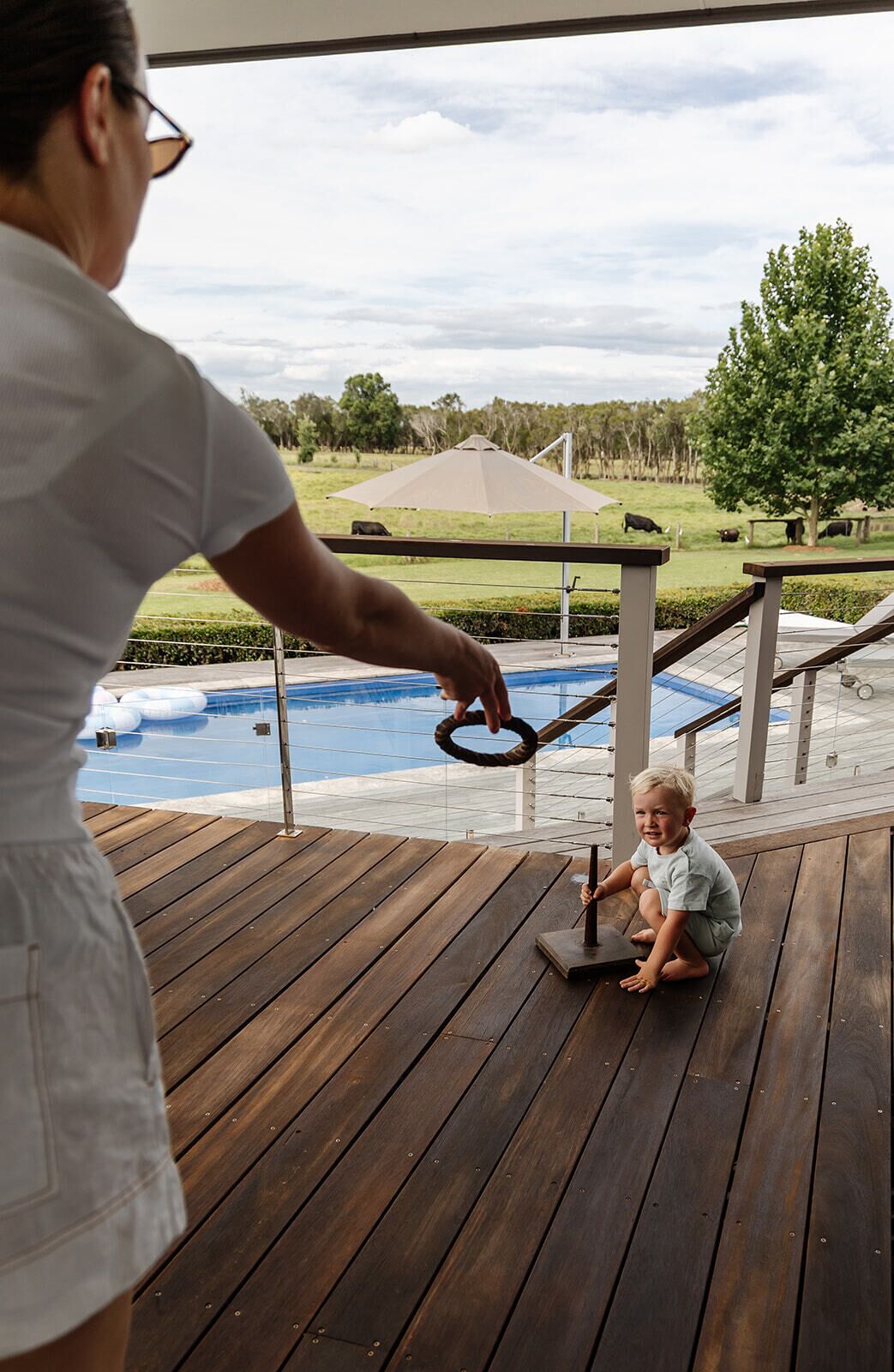 A wooden deck with a pool and a grassy area with trees and a fence in the background.