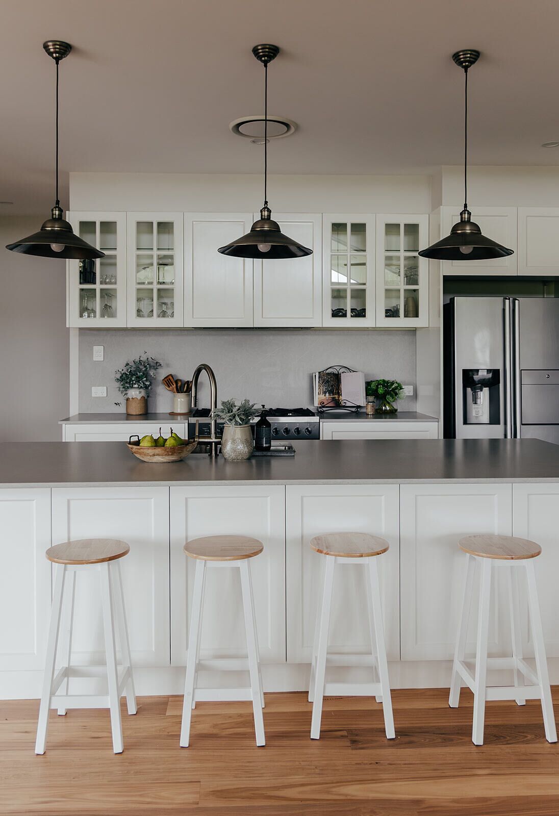 A modern kitchen with white cabinetry, a stainless steel refrigerator, and three bar stools.