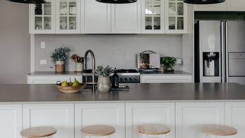 A modern kitchen with white cabinetry, a stainless steel refrigerator, and three bar stools.