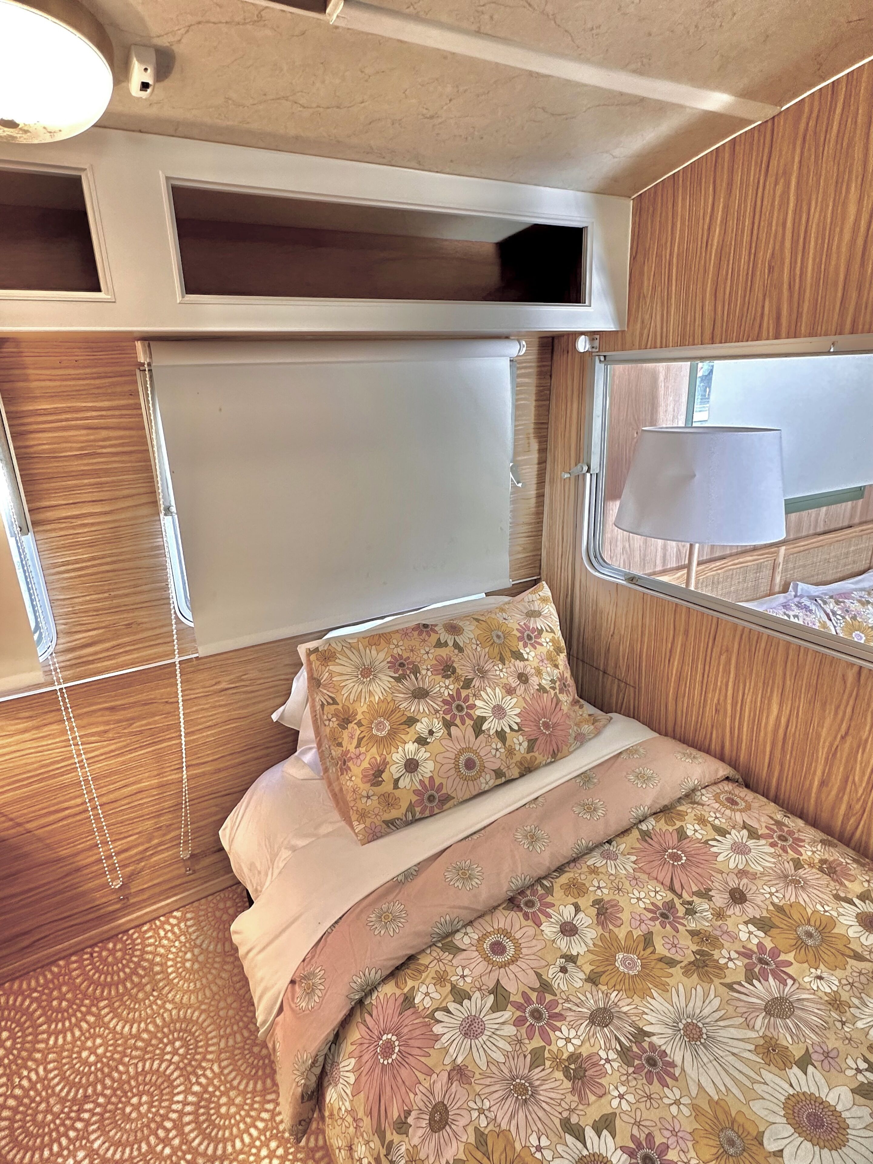 A compact RV bedroom with a bed, a window with a view, and a ceiling light.