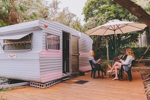 A recreational vehicle with a sliding door, a deck, and an umbrella. - Mornington Peninsula Retro Caravans (Rye)