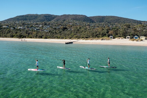 A beach with clear water and people paddleboarding. - Mornington Peninsula Retro Caravans (Rye)