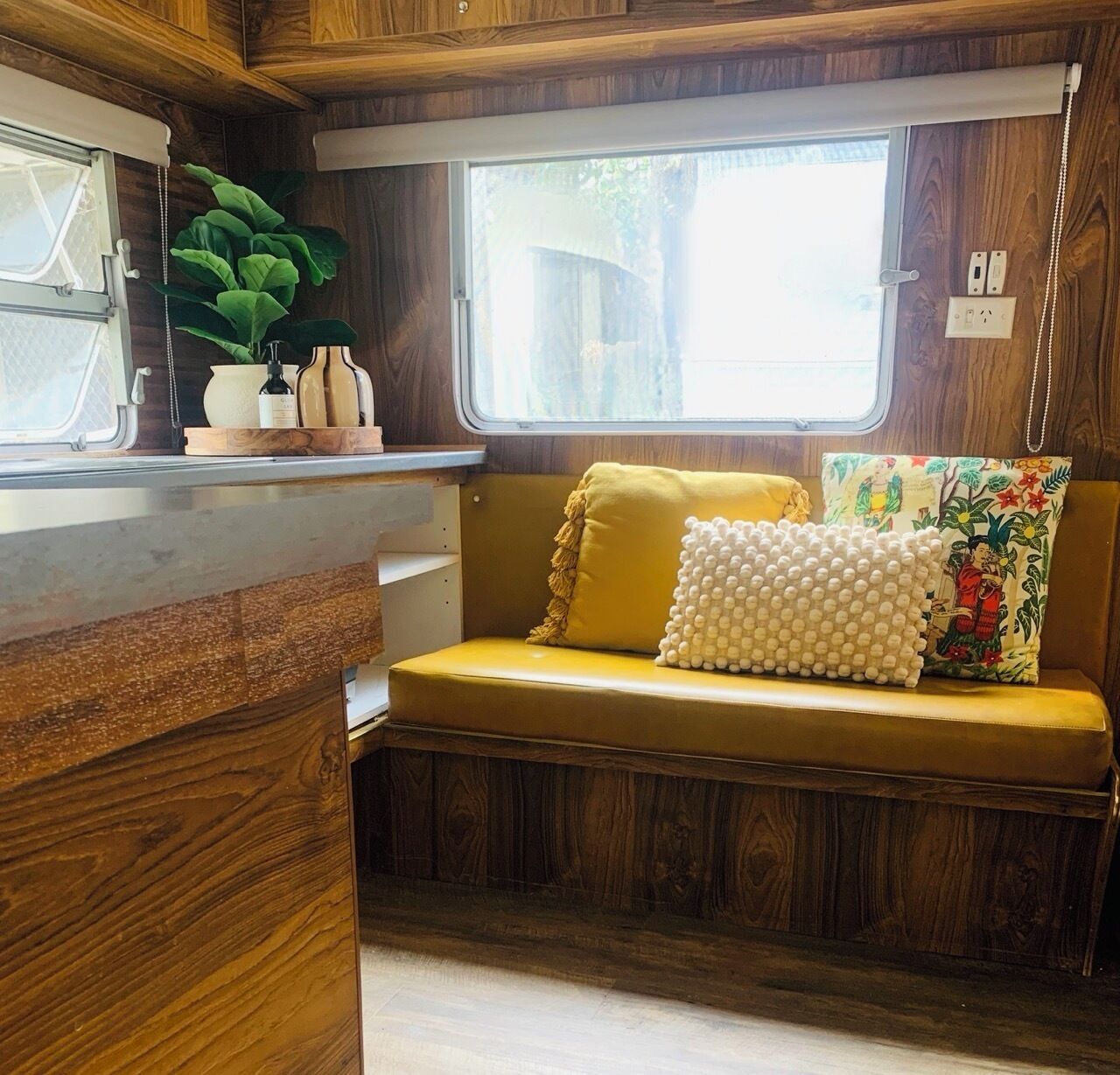 A compact RV interior with a wooden bench, a window, and a small kitchenette area.