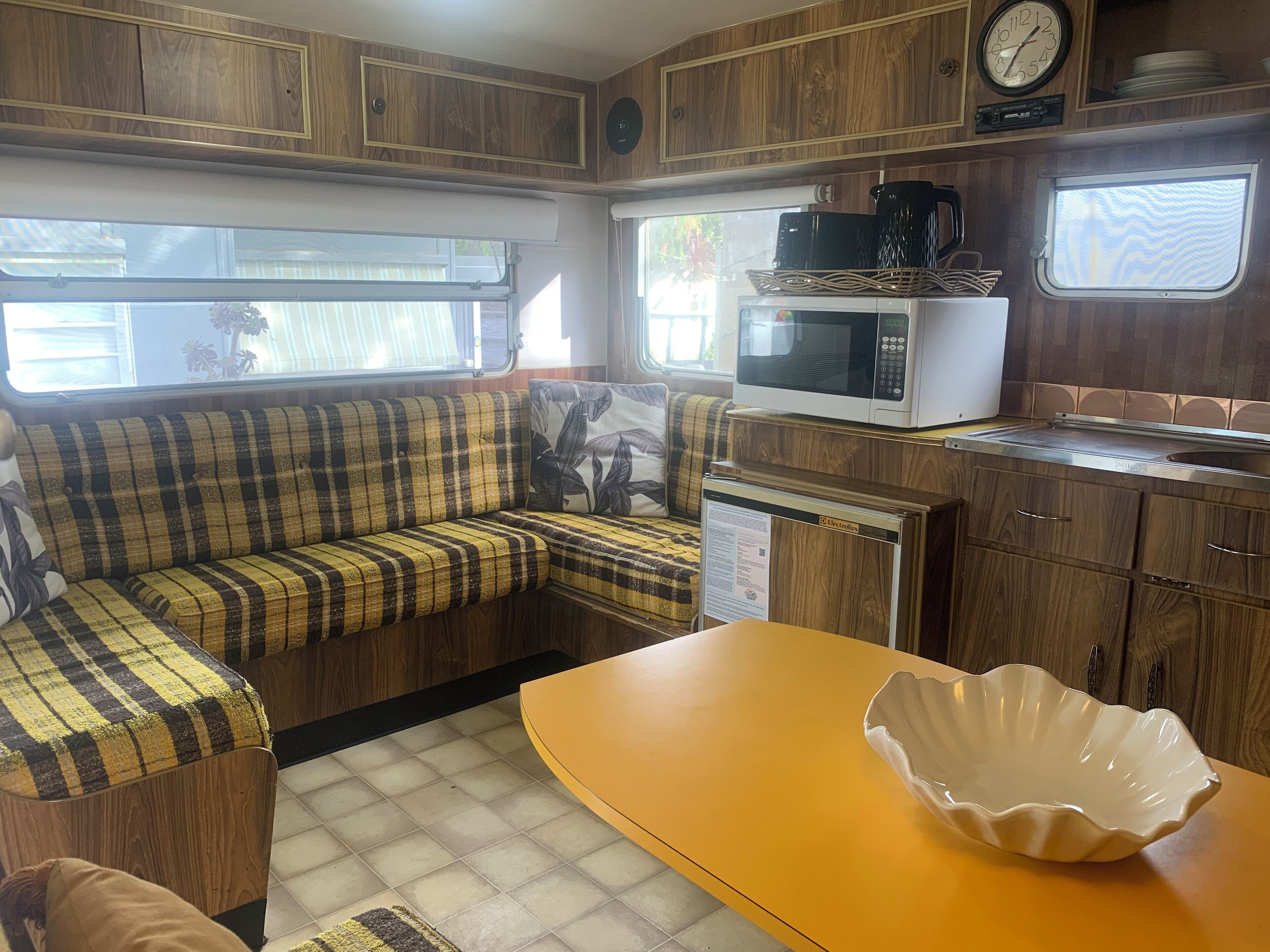 Cocina compacta para autocaravana, con microondas, pileta y comedor con mesa amarilla y un cuenco decorativo.