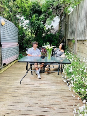 A patio with a table and chairs, surrounded by greenery and a wooden fence. - Mornington Peninsula Retro Caravans (Rye)