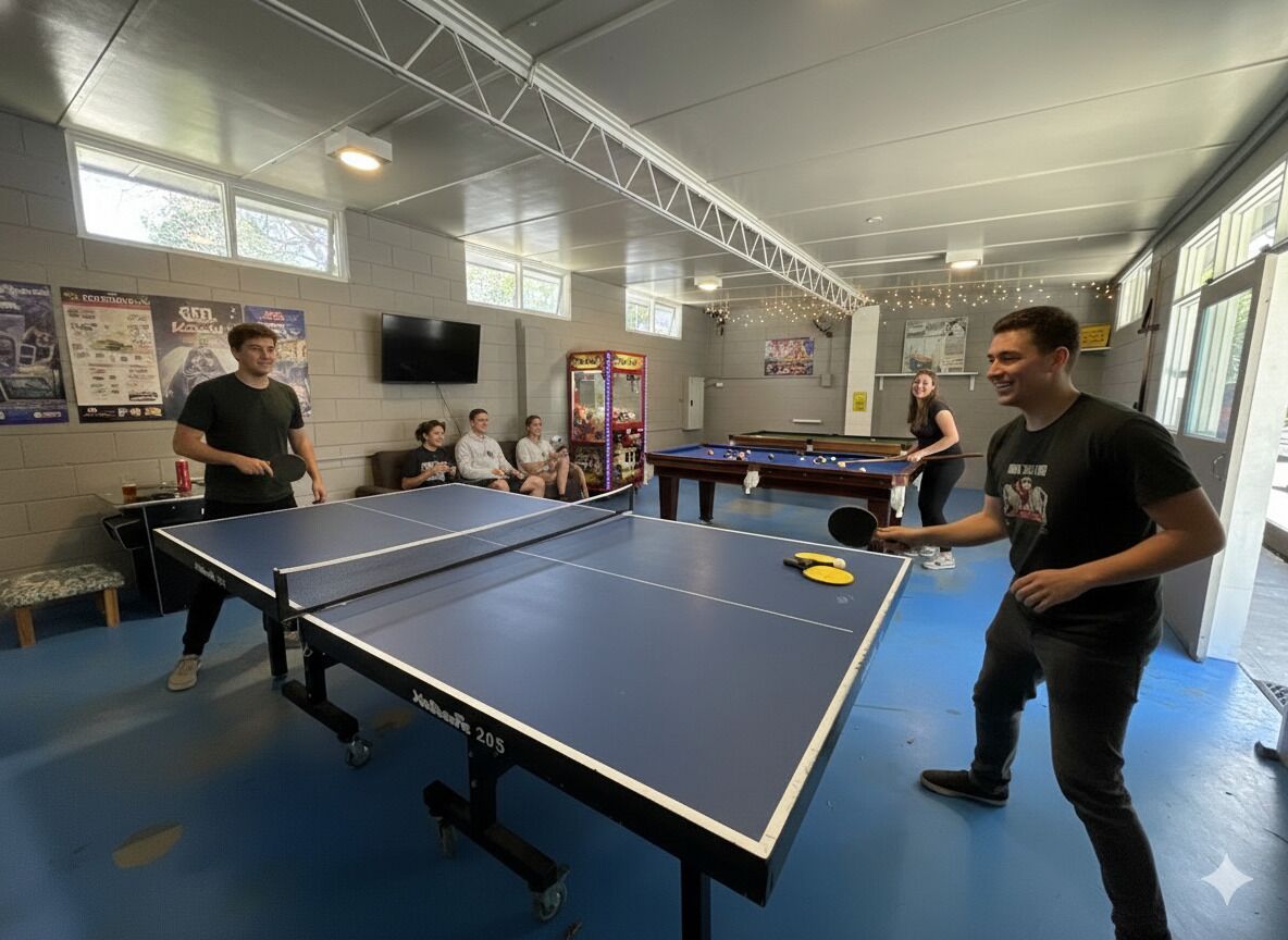 Ein Tischtennistisch in einem Raum mit blauem Boden, einem Billardtisch und Postern an den Wänden.