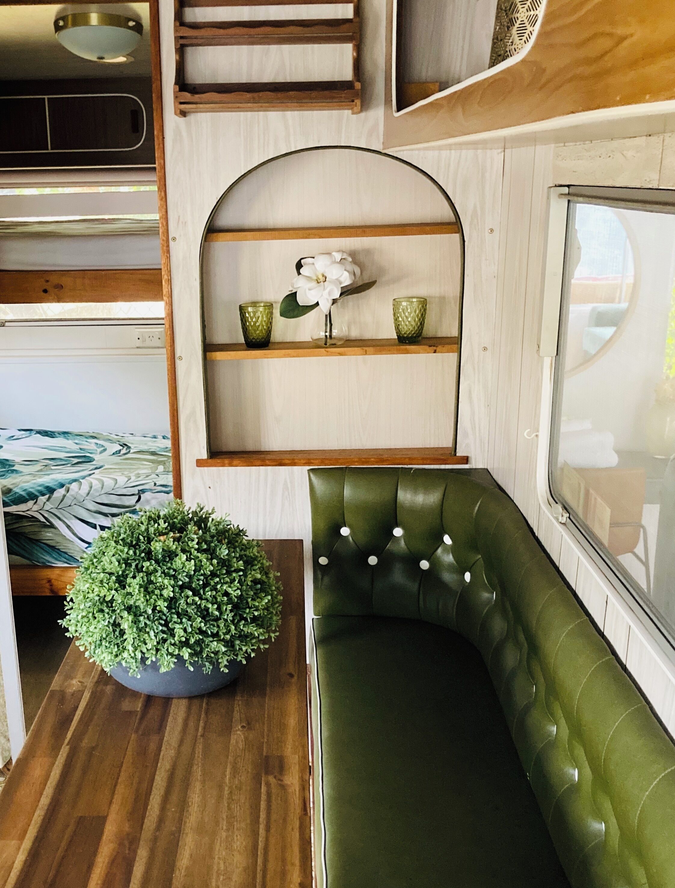 Un interior acogedor con un banco tapizado de verde, una estantería de madera con adornos y una planta en maceta.