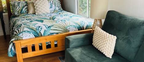 Une chambre à coucher avec un lit en bois, un canapé vert, une grande fenêtre et un climatiseur fixé au mur.