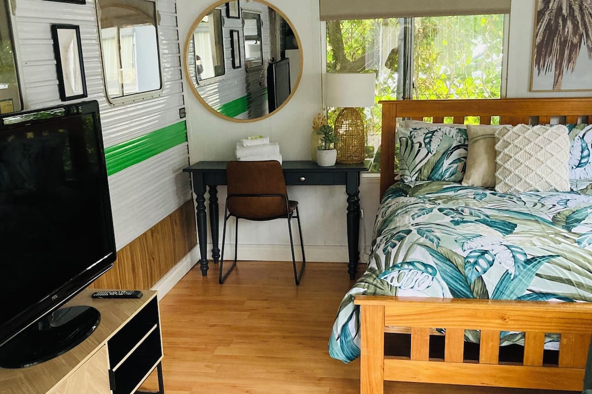 A bedroom with a bed, a desk, a chair, a TV, and a window.