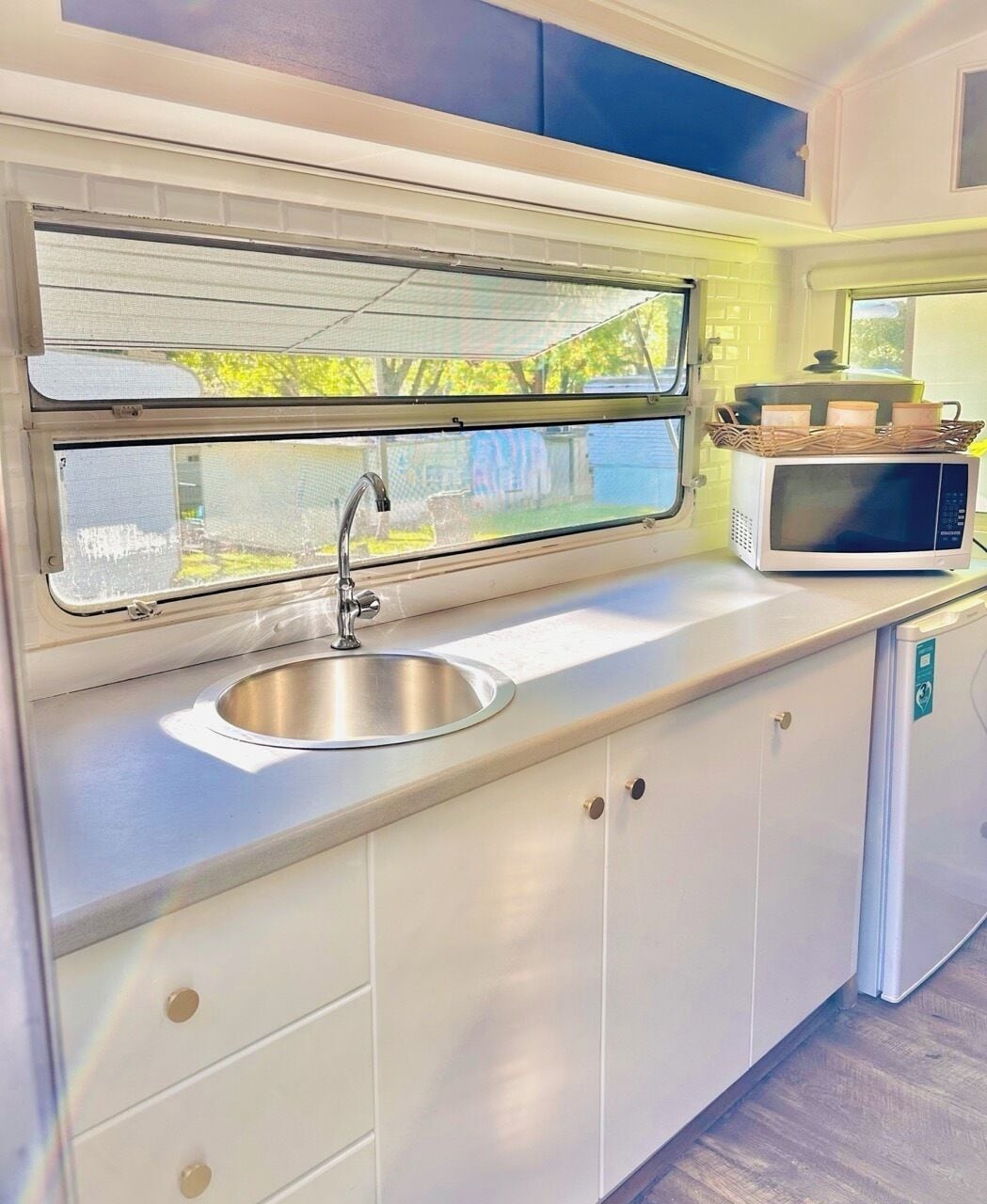 A compact kitchenette with a stainless steel sink, a microwave, and a window above the sink.