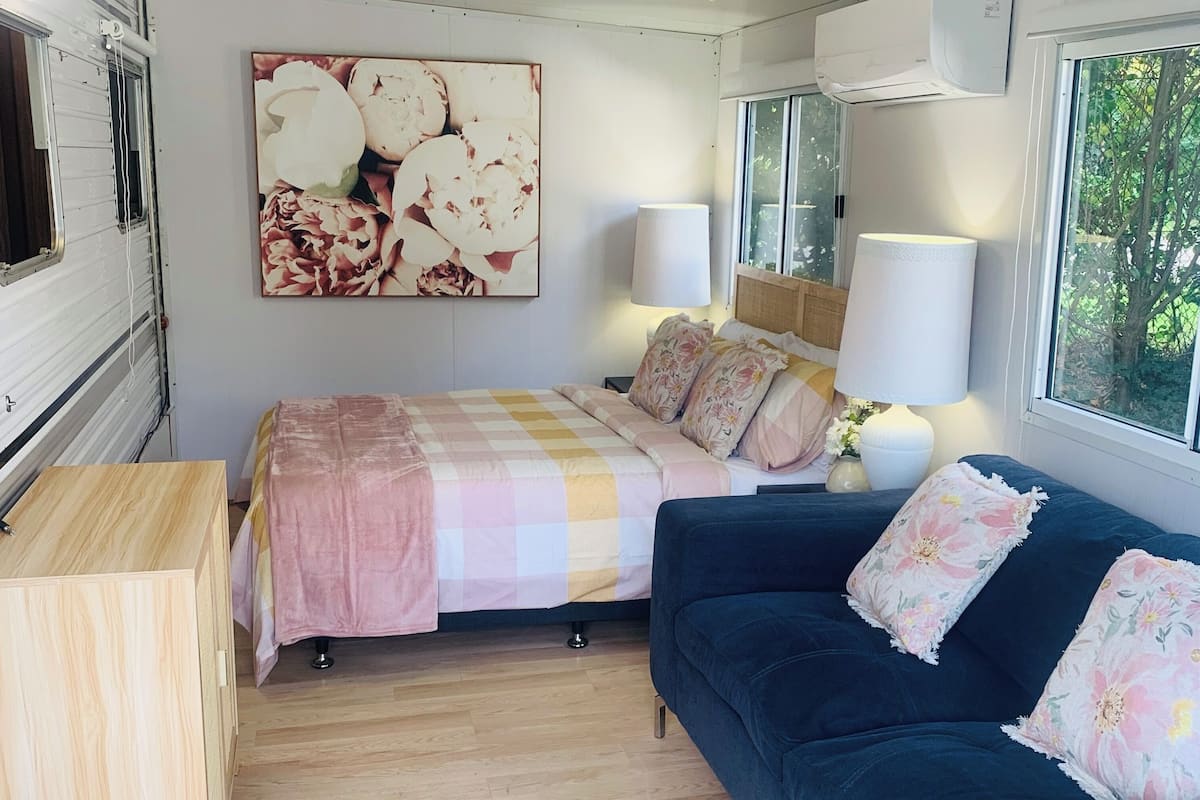 A cozy interior with a bed, a blue sofa, a wooden cabinet, and a large floral artwork on the wall.