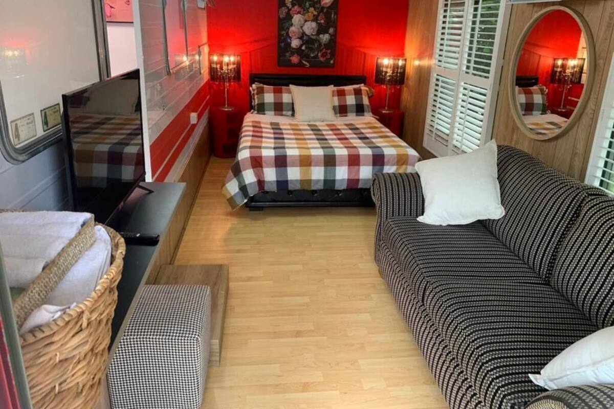 A bedroom with a bed, a sofa, a TV, a mirror, and a window with shutters.