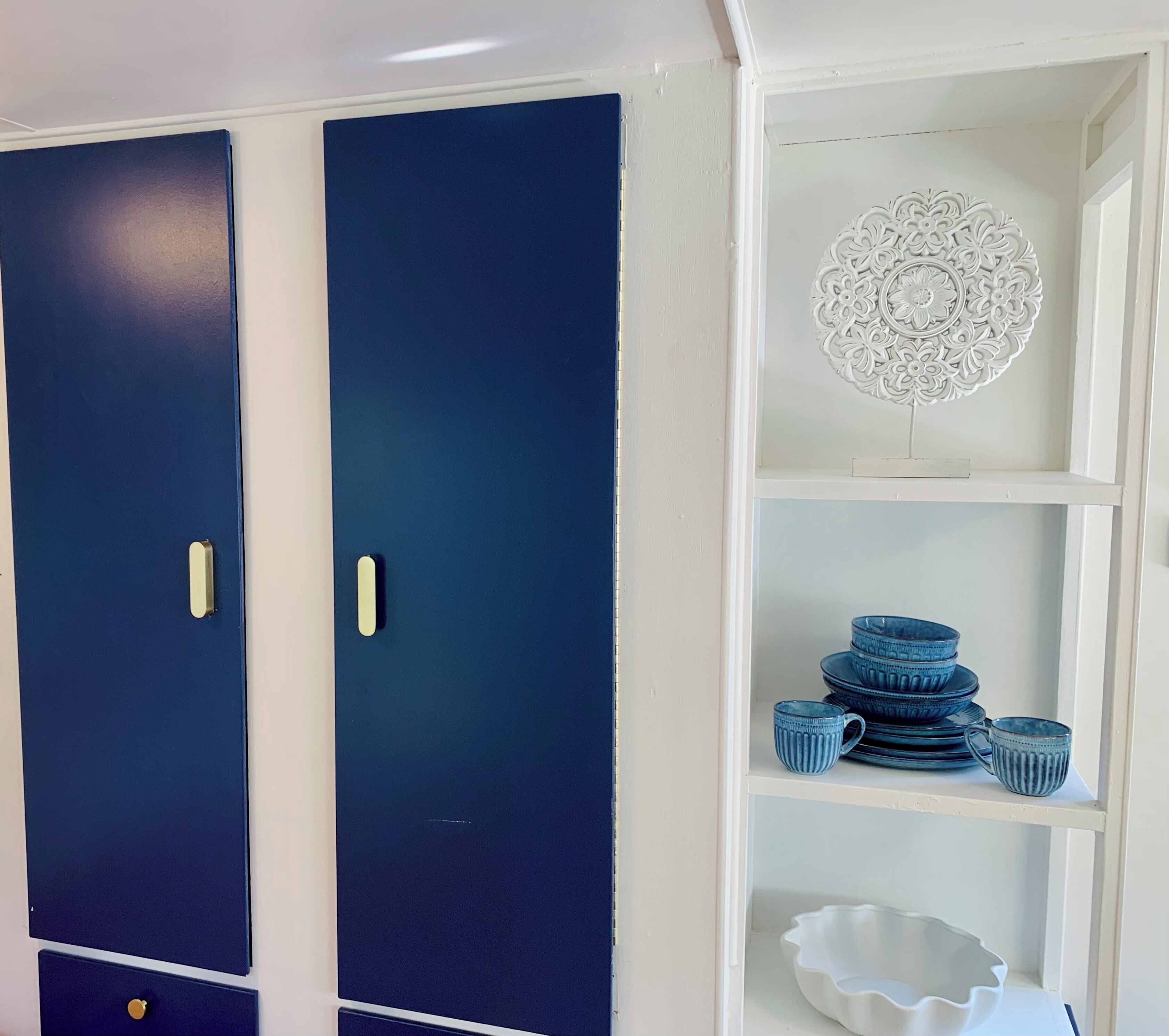 A room with two dark blue doors, a white decorative wall piece, and a shelf with stacked blue dishes and a white bowl.