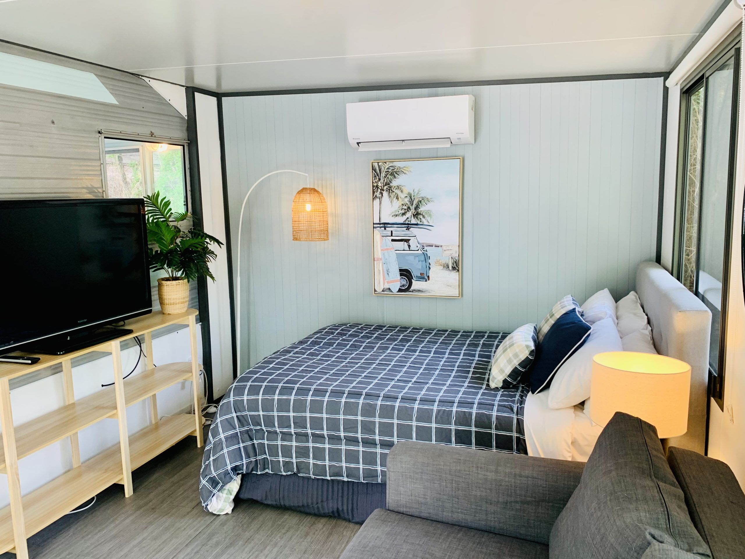 A modern bedroom with a bed, a TV, a wall-mounted air conditioner, a framed picture, and a plant.