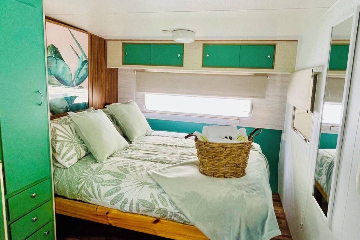 A compact RV bedroom with a bed, a green wardrobe, and a small window.