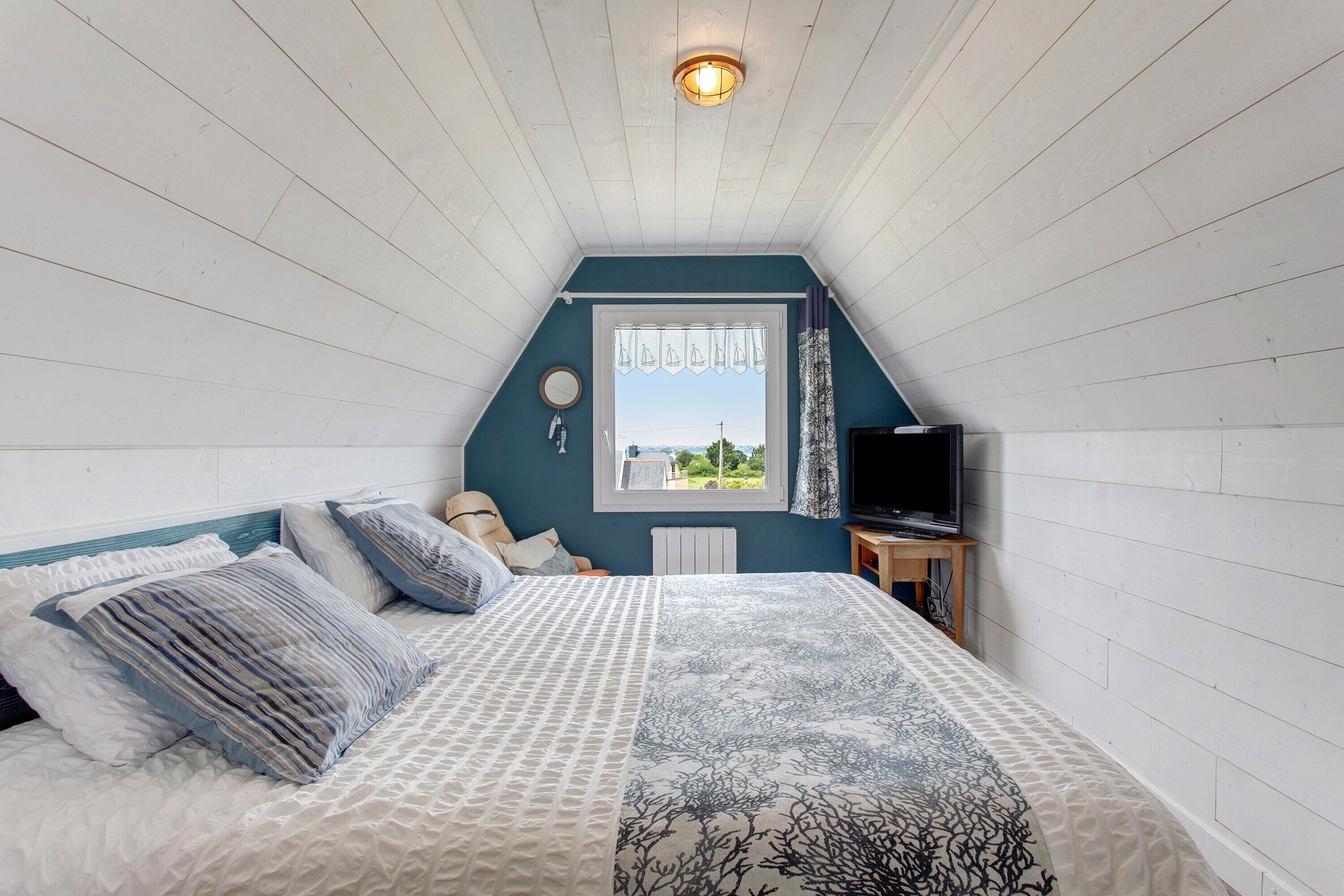 Une chambre à coucher avec un lit, une fenêtre avec des rideaux, un téléviseur et une vue sur l’extérieur.