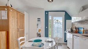 A modern kitchen with wooden cabinets, a dining table with chairs, and a view of the outdoors. - Studio "Port Lazo" with Sea View, Private Terrace and Wi-Fi (Plouézec)