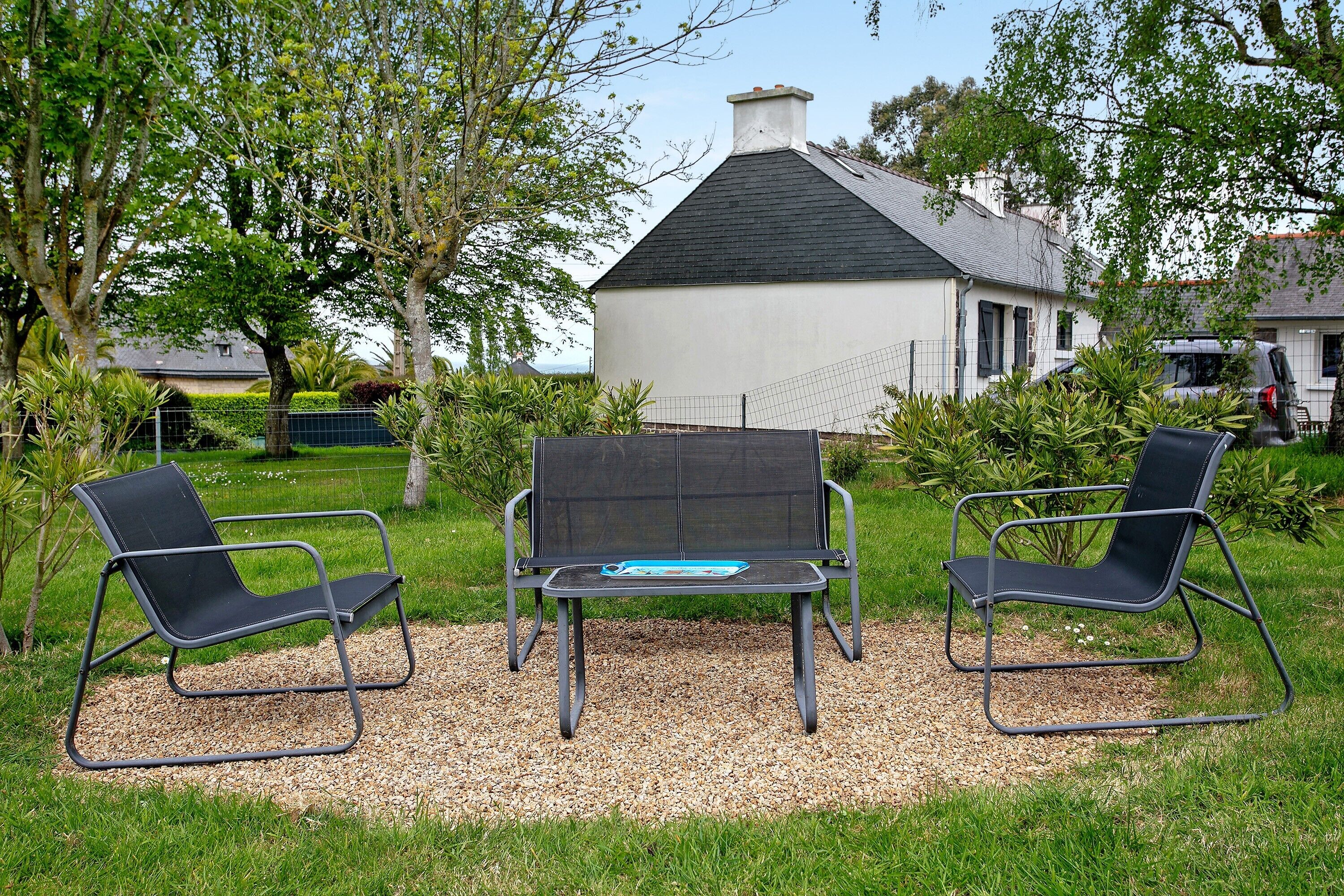 A garden with two black chairs and a table, surrounded by gravel and grass, with a white building in the background.