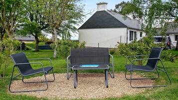 A garden with two black chairs and a table, surrounded by gravel and grass, with a white building in the background.