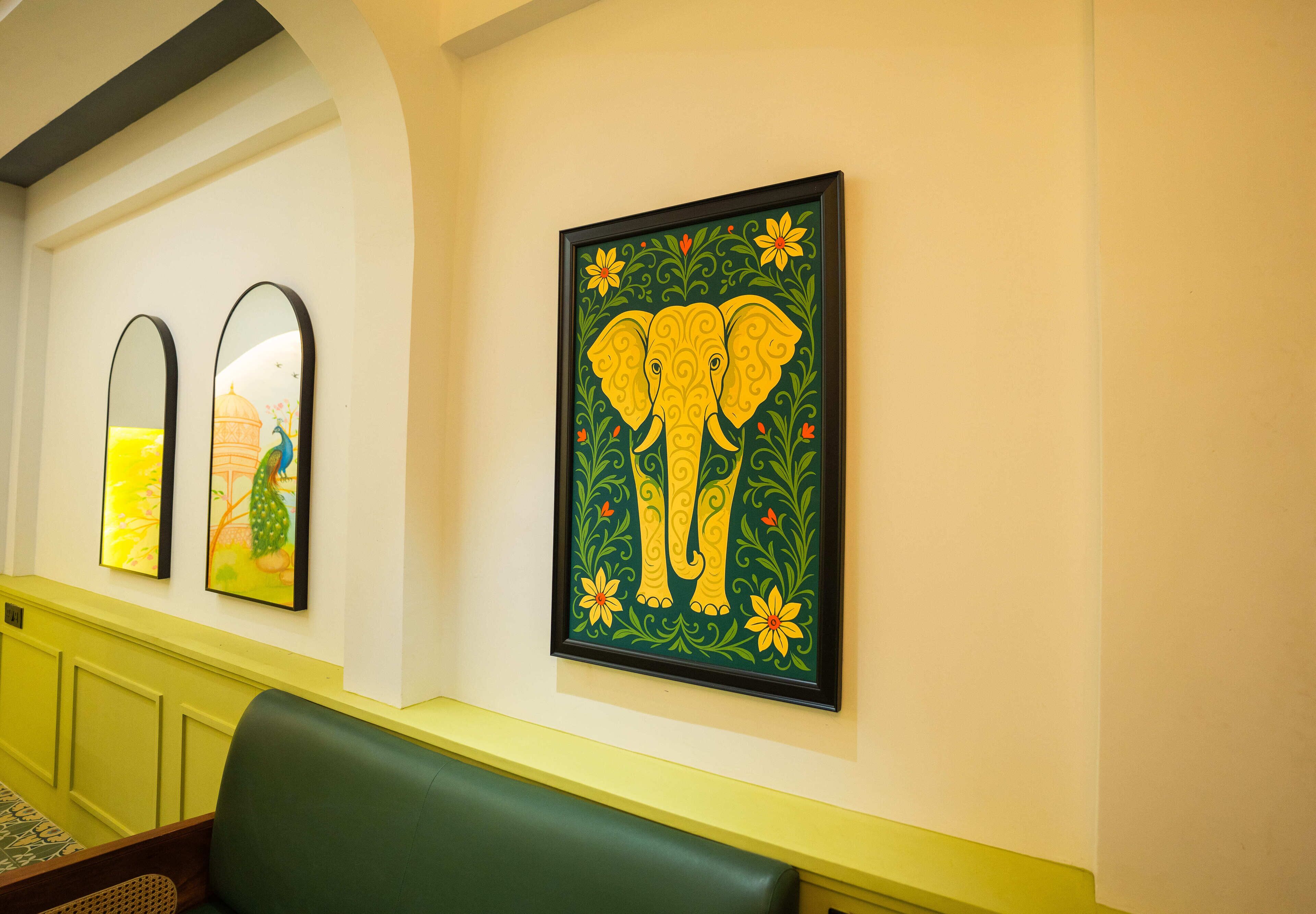 A wall with three framed artworks: one of an elephant, one of a peacock, and one of a building with a dome.