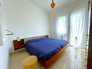 Una camera da letto con un letto, un comodino, una lampada, una finestra con tende e una porta.