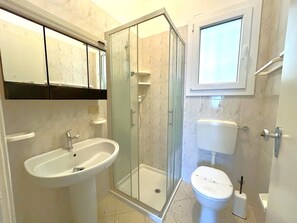 Un bagno con doccia vetro, lavandino, water e specchio sopra il lavandino.