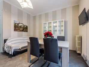 Ein modernes Zimmer mit einem Bett, einem Esstisch mit Stühlen, einer Topfpflanze, einem an der Wand befestigten Fernseher und einer Heizung.