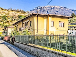 A yellow building with a balcony, a fenced yard, and a mountain in the background. - Beautiful apartment for 4 people with WIFI, TV, balcony and pets allowed (Carlazzo)