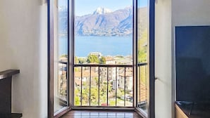Una habitación con un amplio ventanal corredizo que da a un balcón con vistas a un lago y montañas.