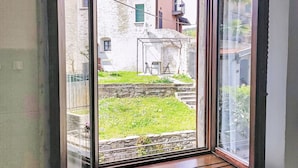 Una habitación con un ventanal grande, un banco de madera y vistas a un muro de piedra y follaje exterior.