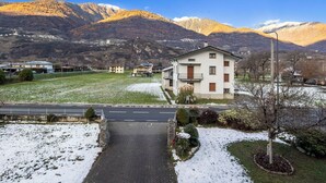 Zona residencial con una casa que tiene balcón, camino de entrada pavimentado y vistas a montañas nevadas.