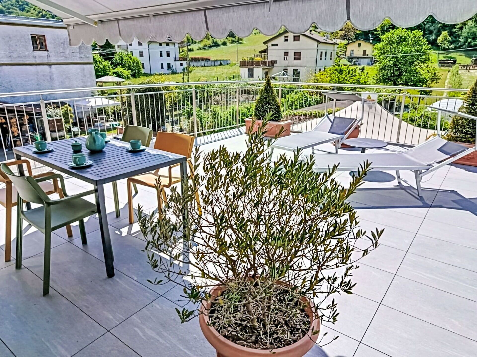 A terrace with a table set for tea, chairs, a potted plant, and lounge chairs.