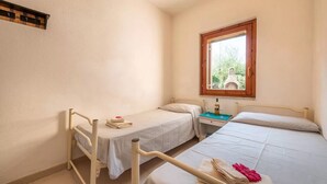 A small, clean room with two single beds, a window with a view, and a bedside table with a lamp. - Perfectly Located Flat in San Teodoro (San Teodoro)