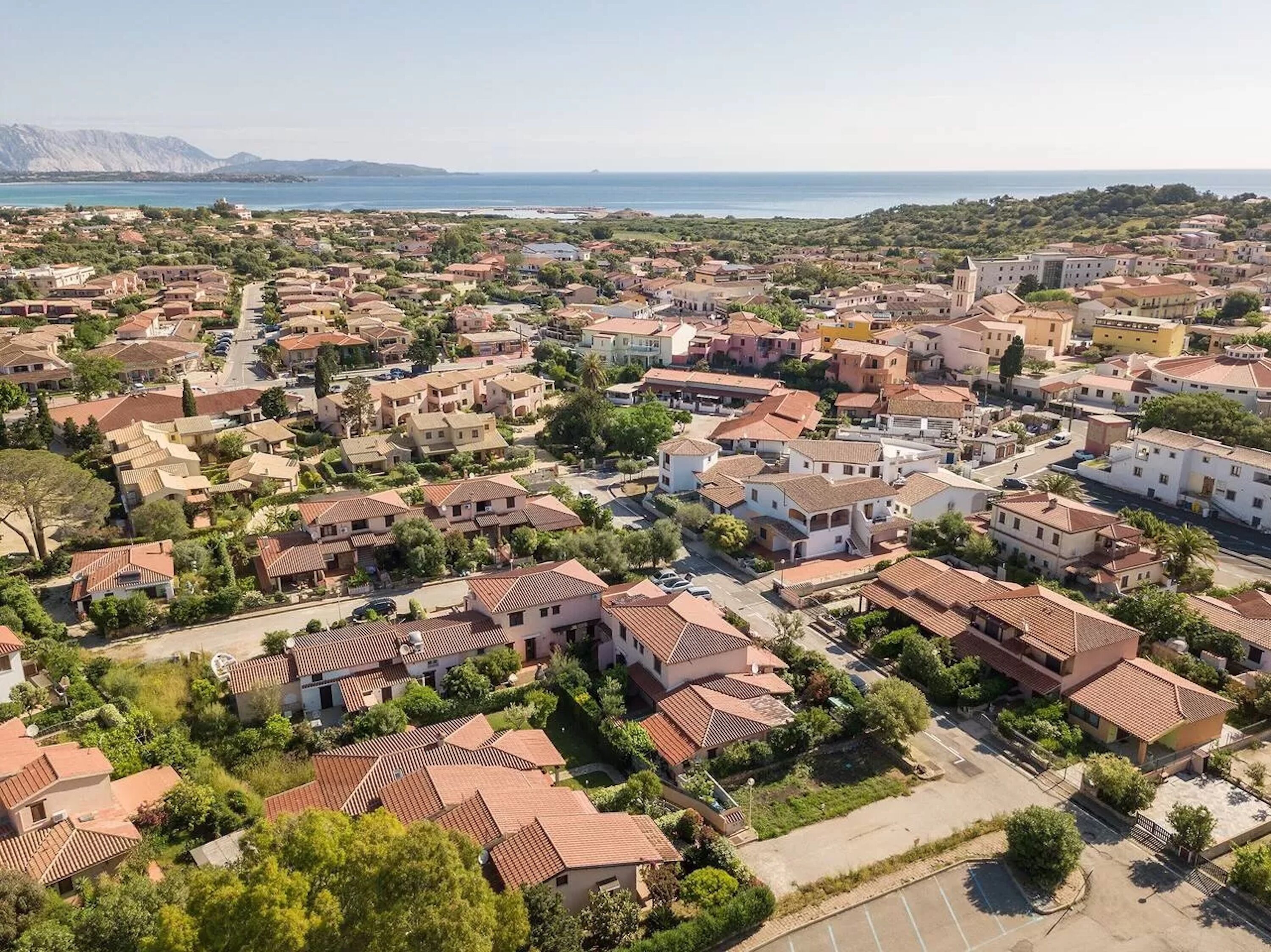 Vue aérienne d’une zone résidentielle côtière, avec des maisons, des routes et une étendue d’eau en arrière-plan.