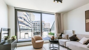 Un salon moderne avec une grande fenêtre, un canapé, un fauteuil et une petite table.