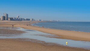 Une vaste plage de sable fin, une mer calme, quelques personnes et des bâtiments qui se dessinent à l’horizon.