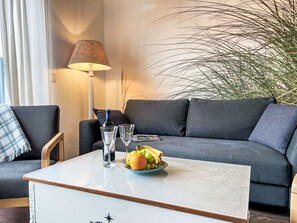Una sala de estar moderna con un sofá gris, una mesa de centro blanca, una lámpara y una planta en maceta.