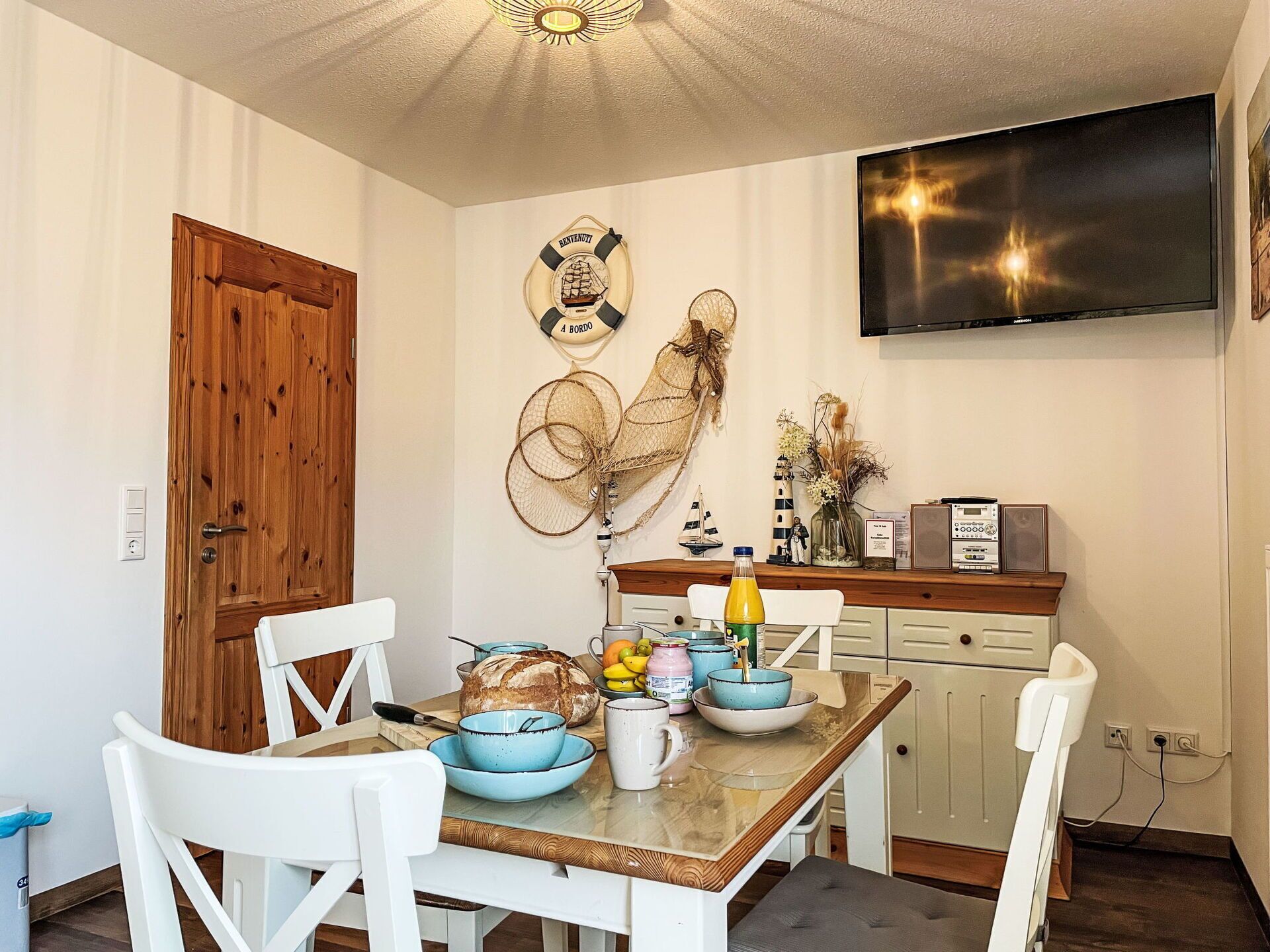 Un coin repas avec une table en bois, des chaises blanches et un téléviseur fixé au mur.
