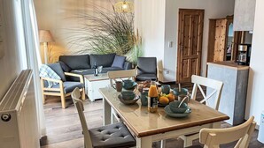 A cozy living room with a sofa, chairs, a dining table with bowls and fruits, a coffee machine, and a wooden cabinet. - Nice apartment for 2 people with WIFI, TV and terrace (Ostseebad Kühlungsborn)